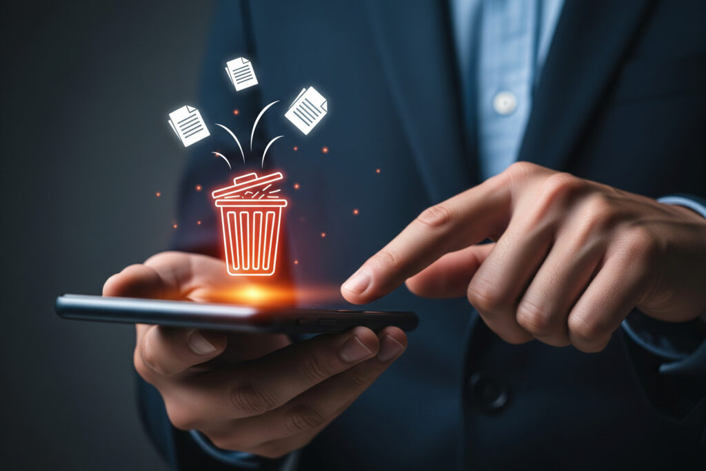 Hands hold a smartphone with a glowing trash can icon and papers flying out, symbolizing delete or discard files on mobile.