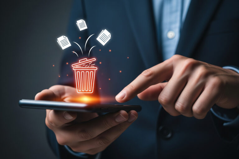 Hands hold a smartphone with a glowing trash can icon and papers flying out, symbolizing delete or discard files on mobile.